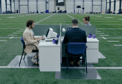 three people sit at white desks at an indoor football field